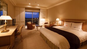Quarto de hotel com cama grande, duas cadeiras, escrivaninha com luminária, TV e varanda com vista.