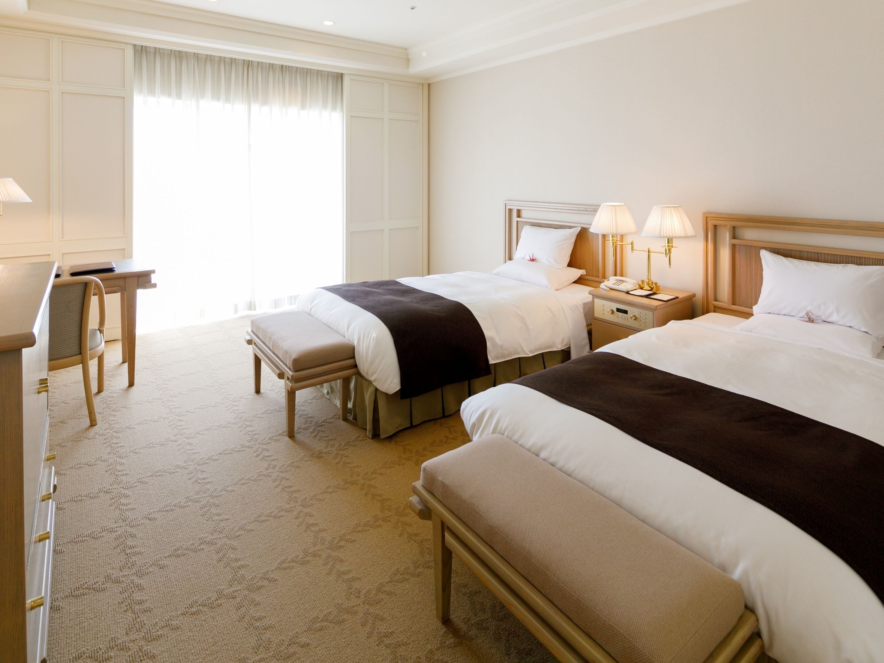 A hotel room with two beds, a desk, and a chair.