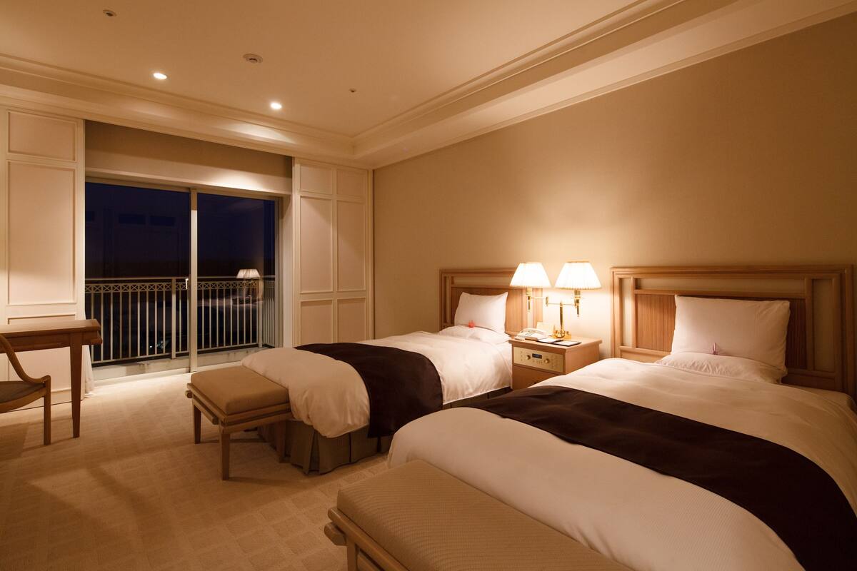 A hotel room with two beds, a desk, and a balcony.