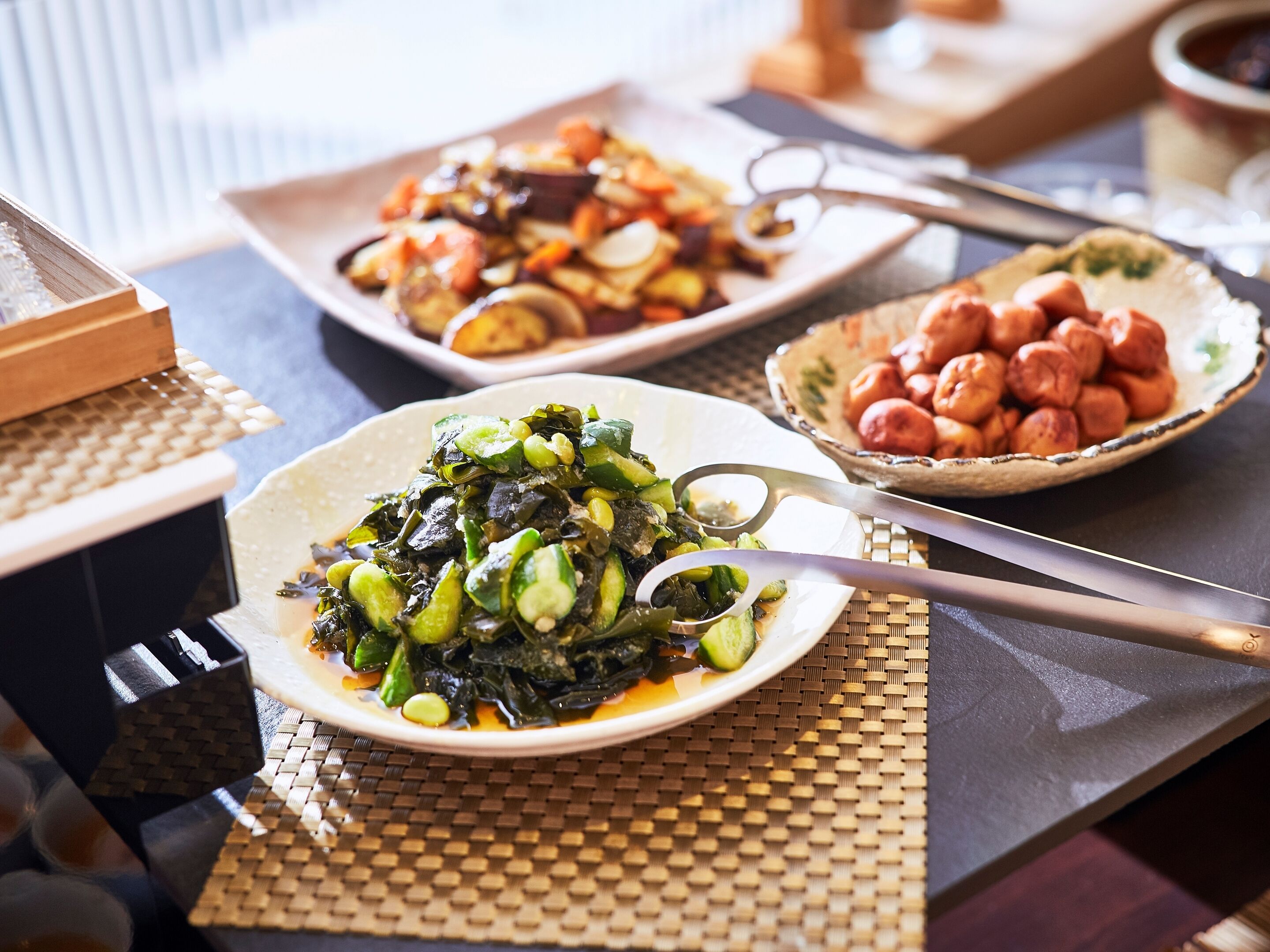 A dining table with various dishes, including a plate of greens, a bowl of peanuts, and a dish with vegetables.