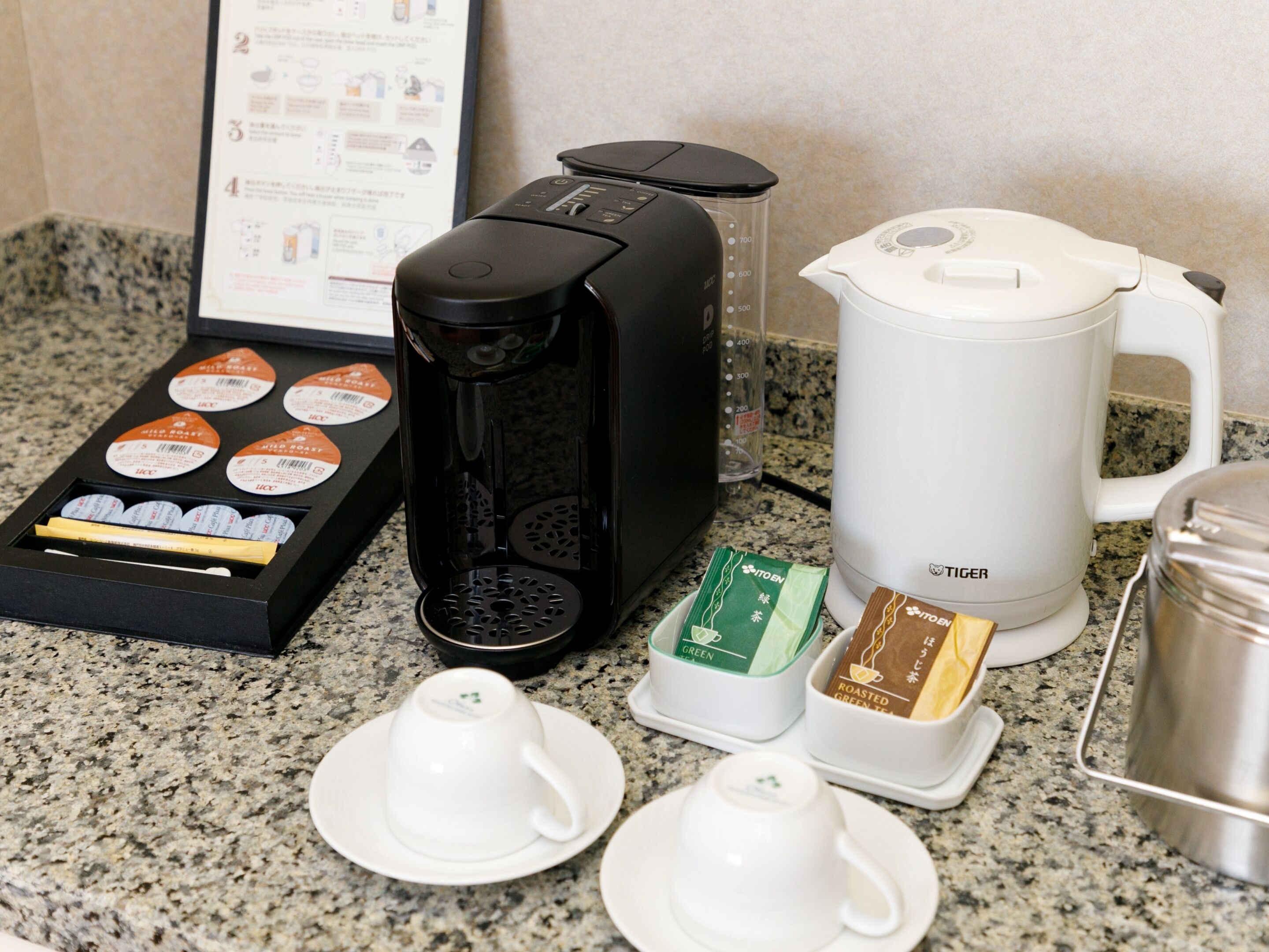 A coffee station with a coffee maker, a kettle, and tea packets on a granite countertop.