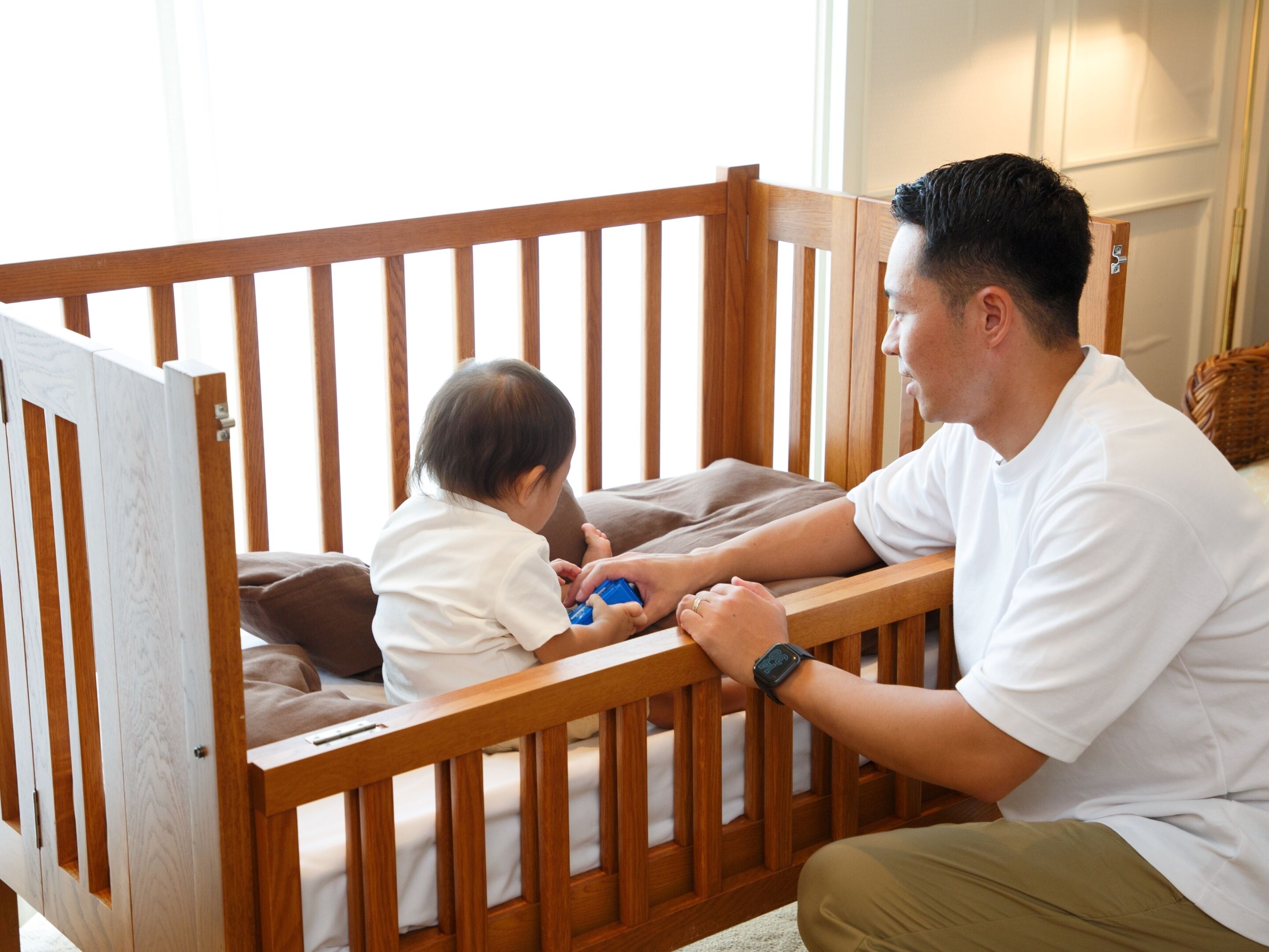A wooden crib with a baby and an adult.