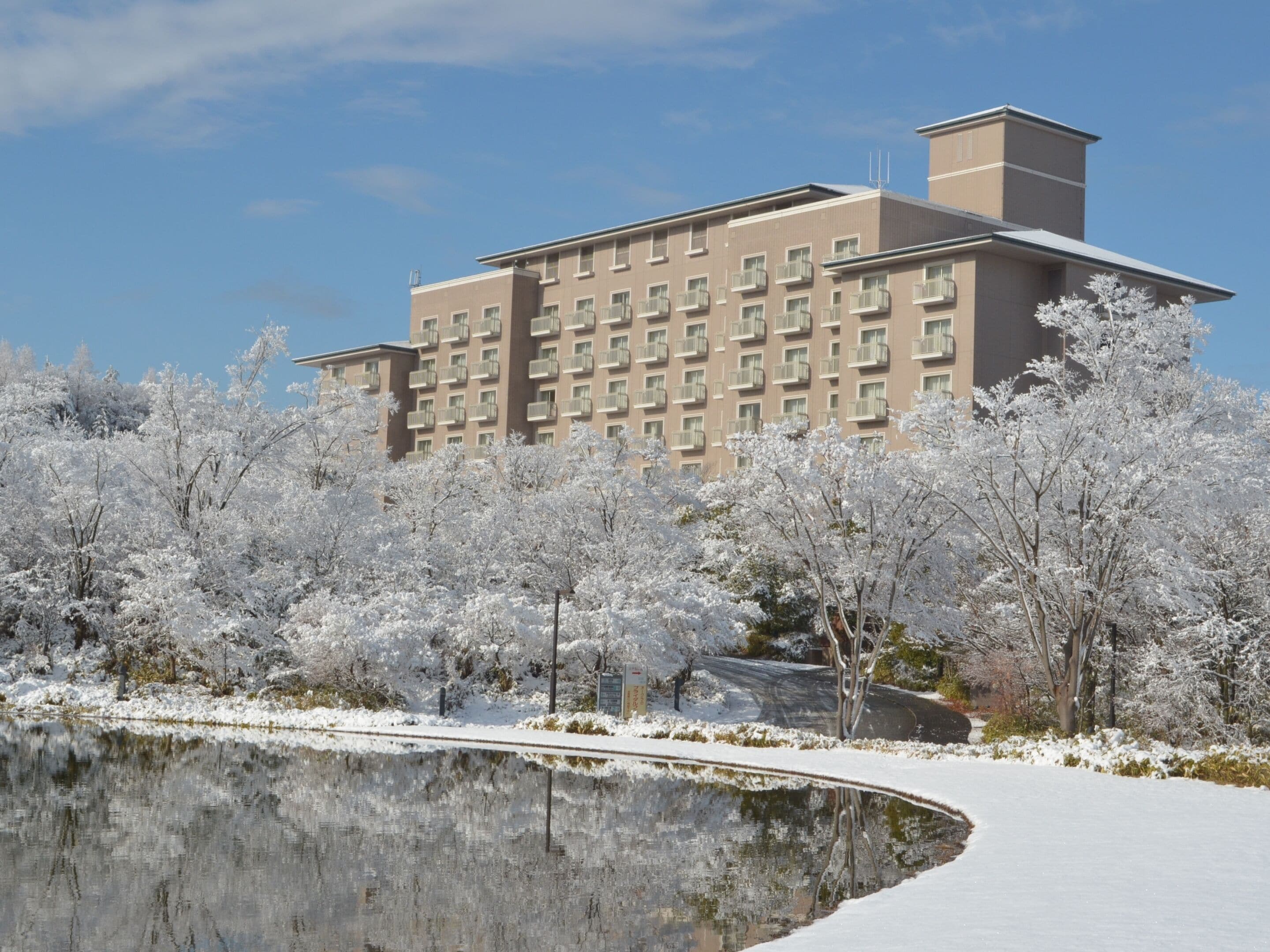A modern hotel with a symmetrical facade, multiple balconies, and a reflective water feature in the foreground.