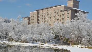 A modern hotel with a symmetrical facade, multiple balconies, and a reflective water feature in the foreground.