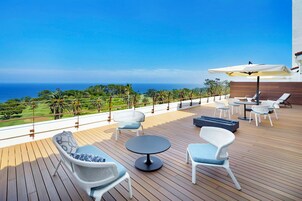 A deck with wicker chairs and a table, overlooking a golf course and the ocean.