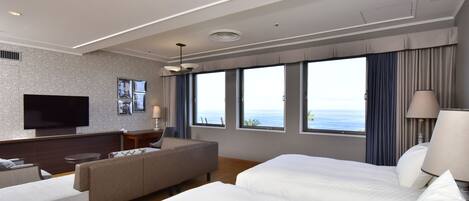 A modern hotel room with a large bed, a sofa, a TV, and a view of the sea.