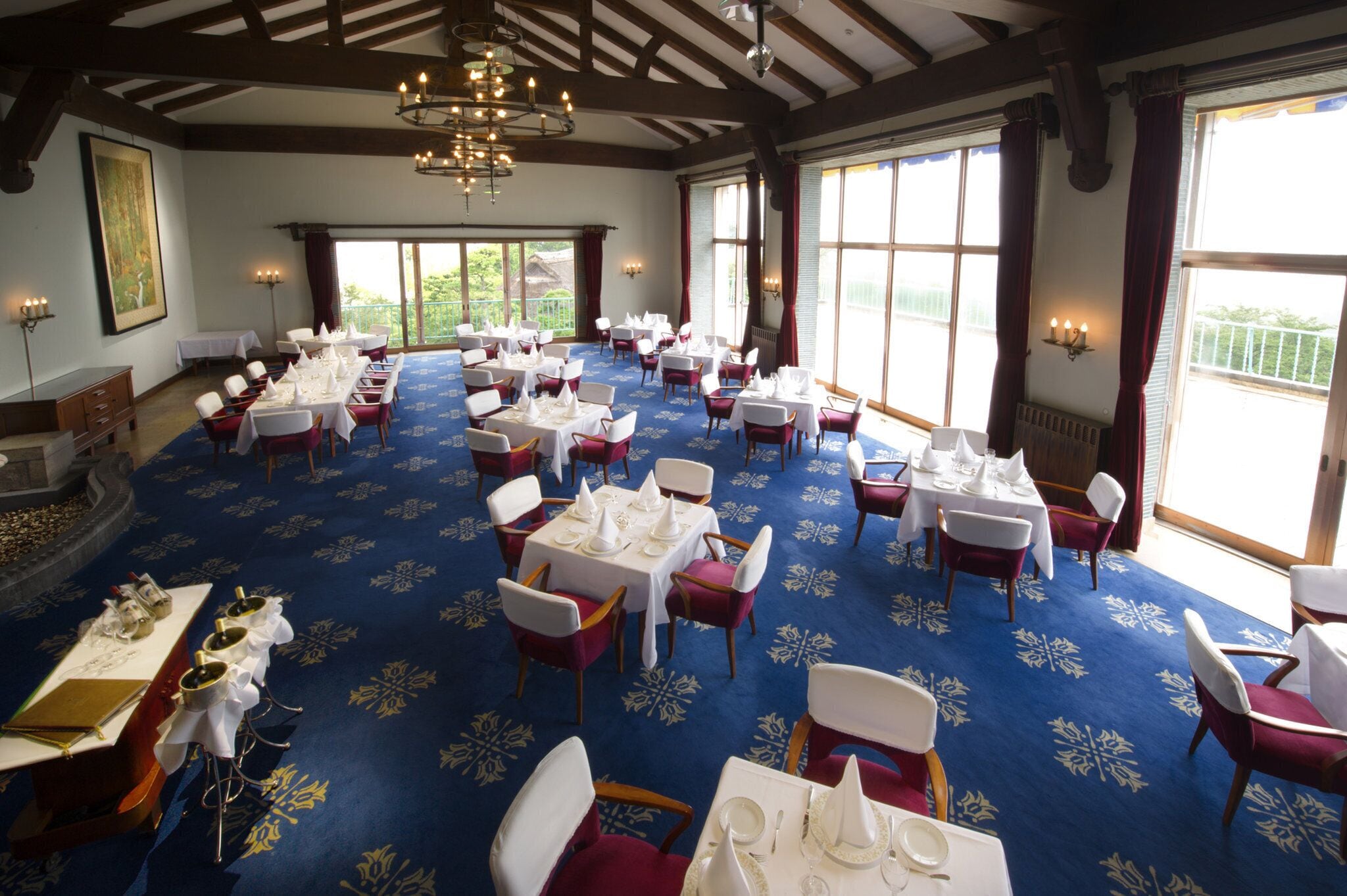Une salle de banquet avec des tables dressées pour le repas, de grandes fenêtres et un lustre.