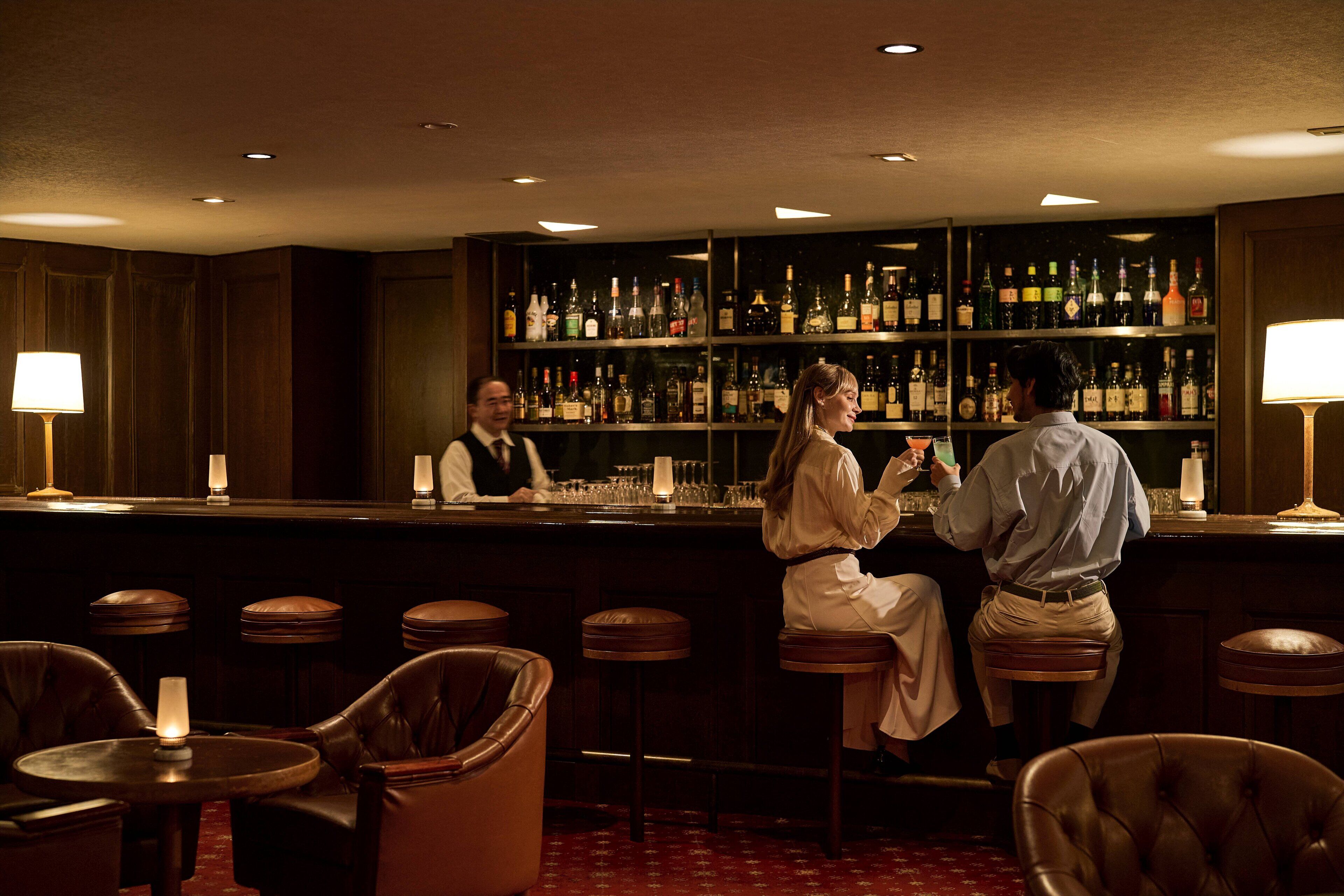 A bar area with leather chairs, a bar counter, and shelves stocked with bottles.