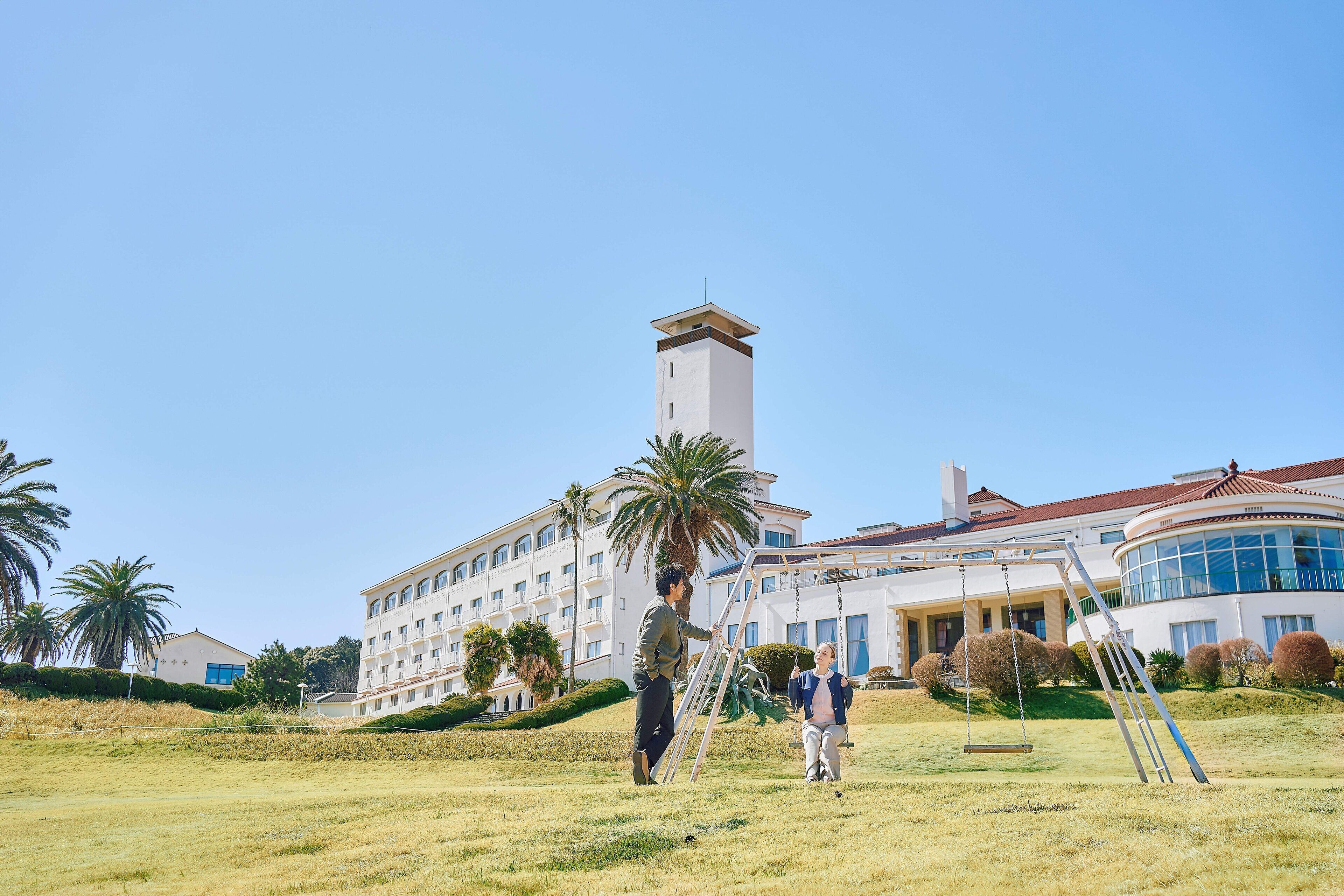 A large building with a prominent tower, a well-maintained lawn, and palm trees.