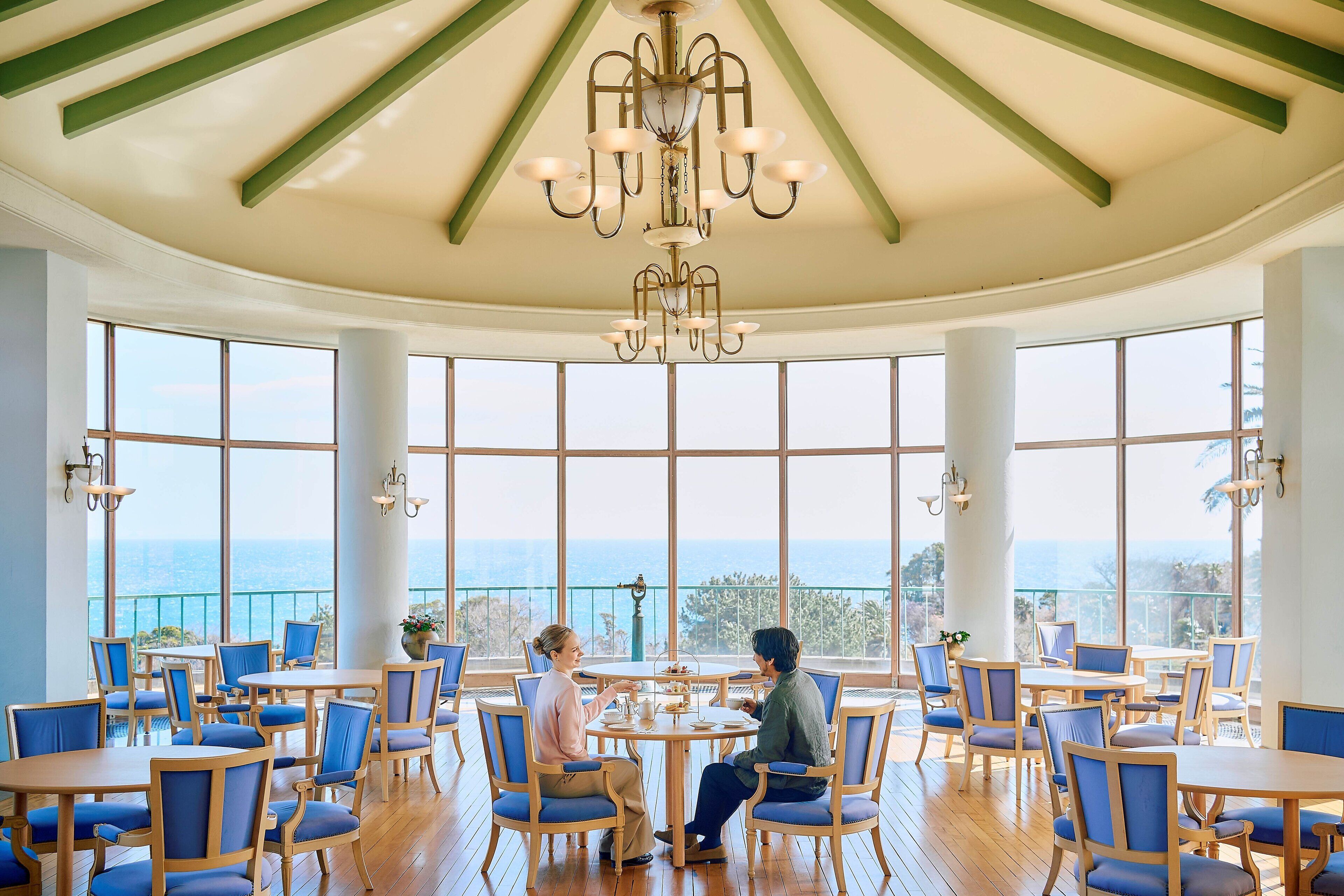 Un comedor amplio con ventanas grandes, una araña y mesas y sillas de madera.