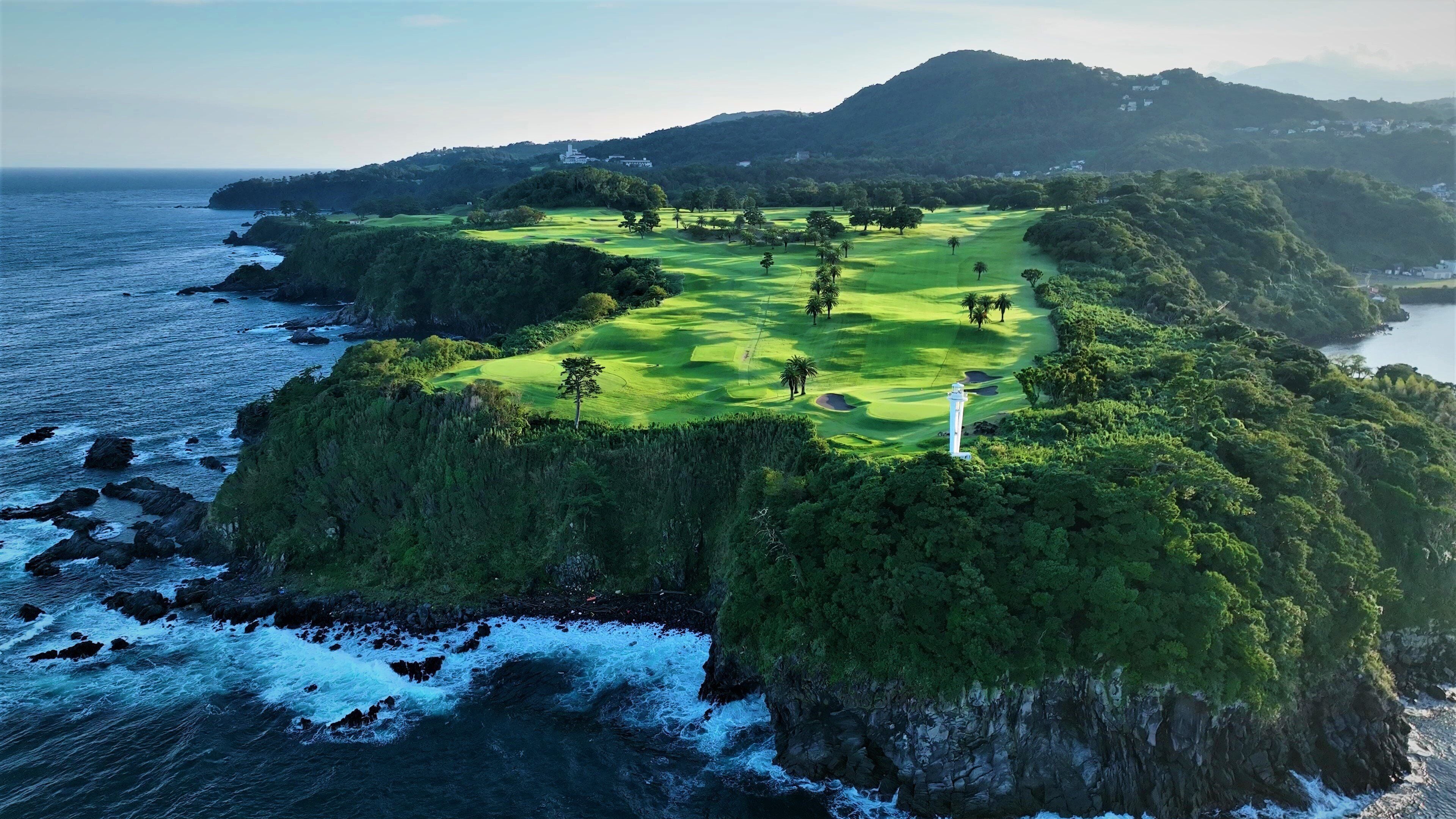 A coastal golf course with lush greenery, a lighthouse, and rocky cliffs.