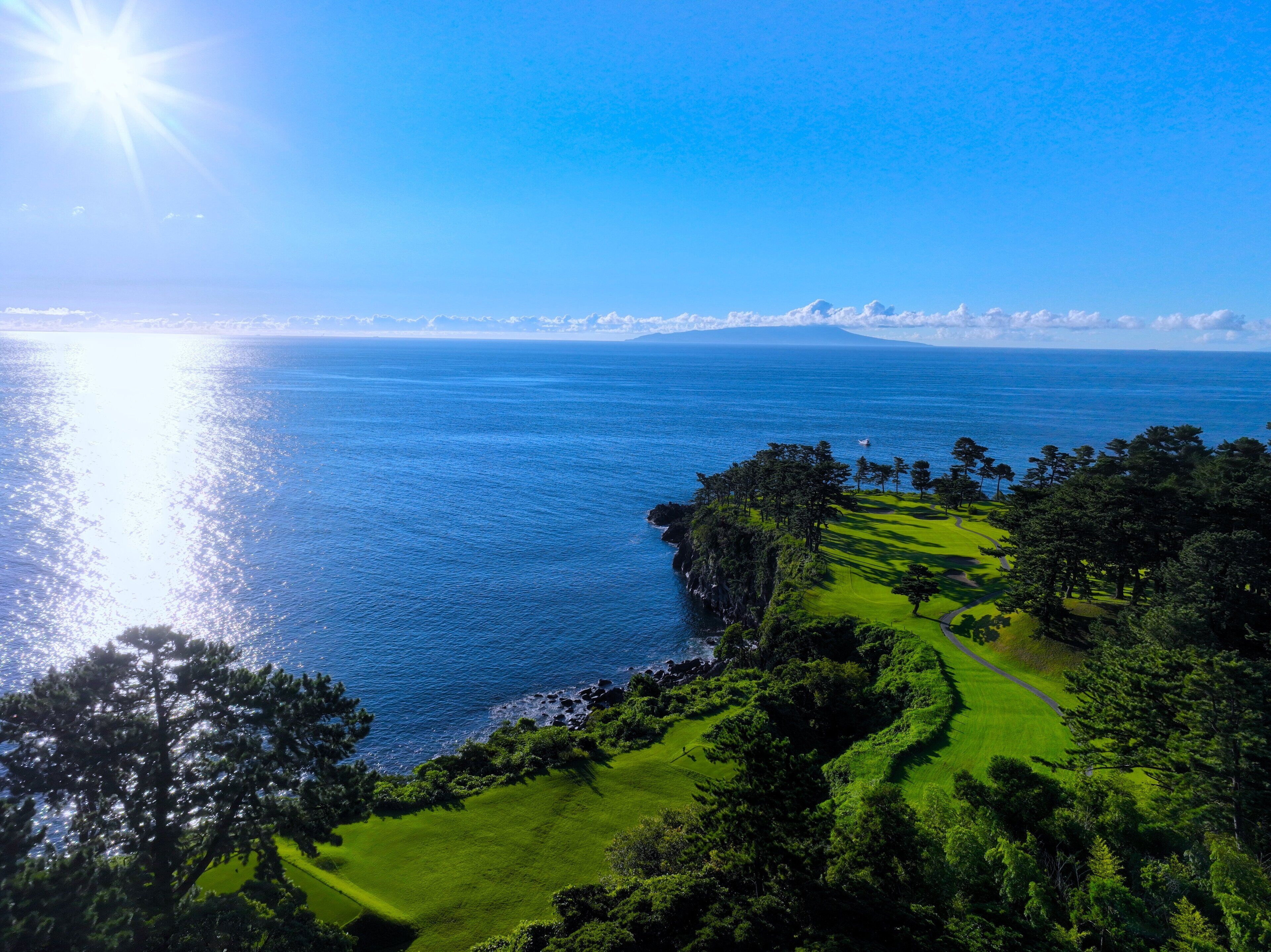 A coastal landscape with a golf course, clear skies, and a view of the ocean.
