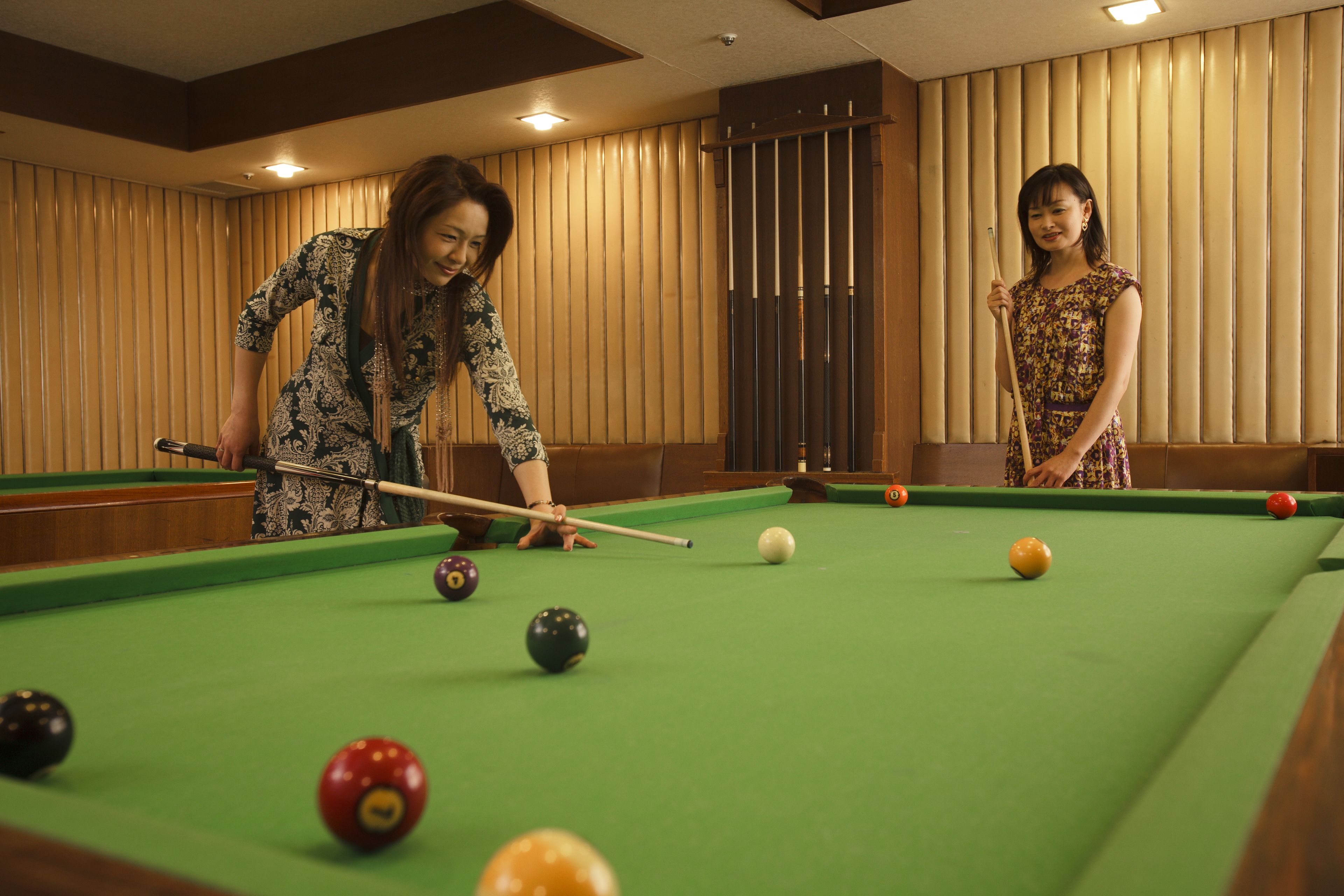 A pool table with balls and cues, wooden paneling, and a ceiling light fixture.