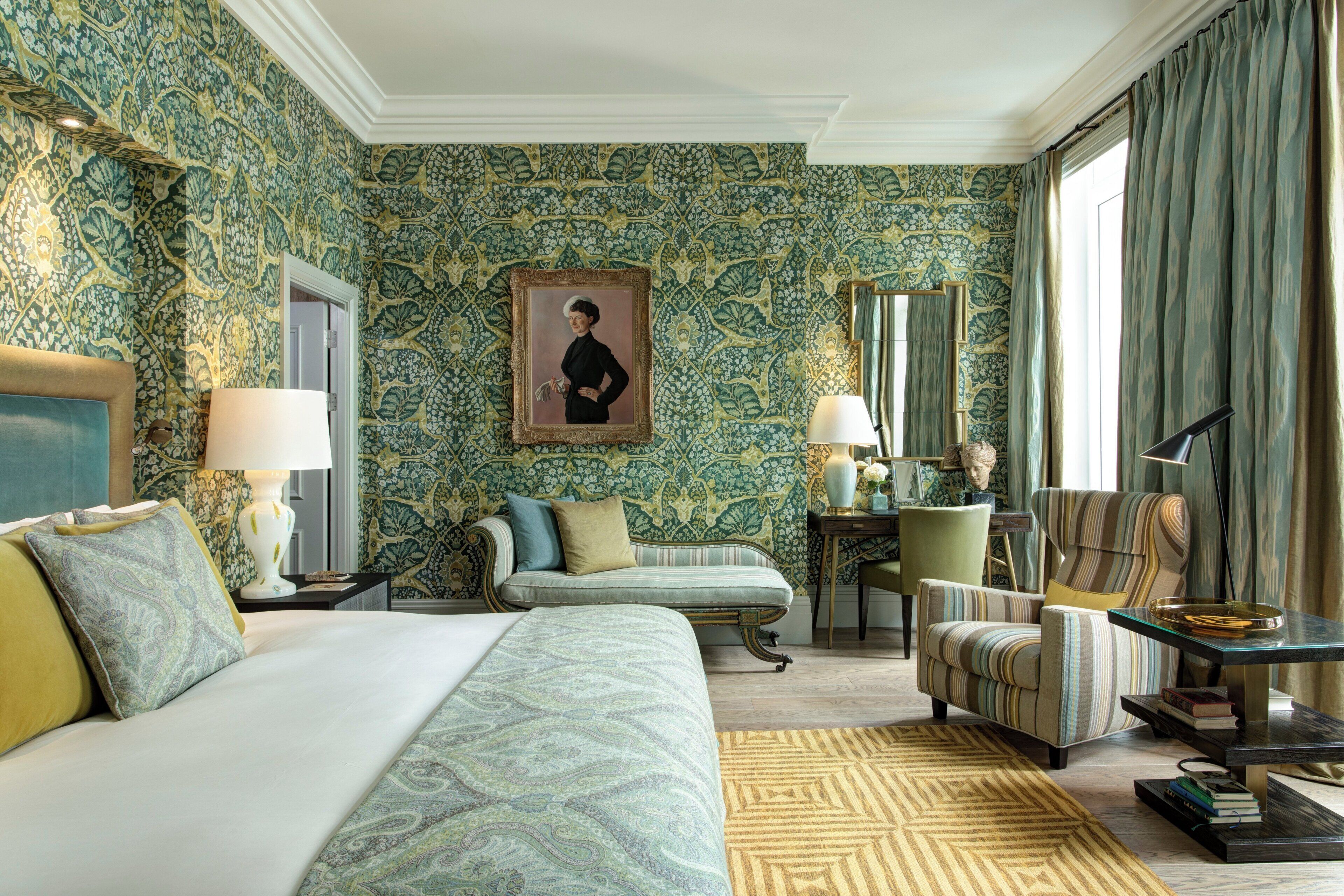 A hotel room with a large bed, a sofa, a chair, a desk with a lamp, and a painting on the wall.