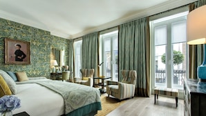 A hotel room with a large bed, two armchairs, a small table, and a bench. There is a window with curtains, a lamp, and a framed picture on the wall. - Brown's Hotel, a Rocco Forte Hotel (London)