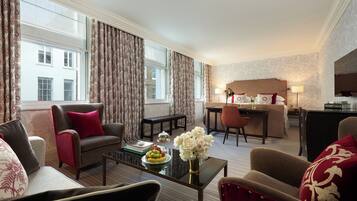 A hotel room with a sofa, armchairs, a dining table, and a desk.