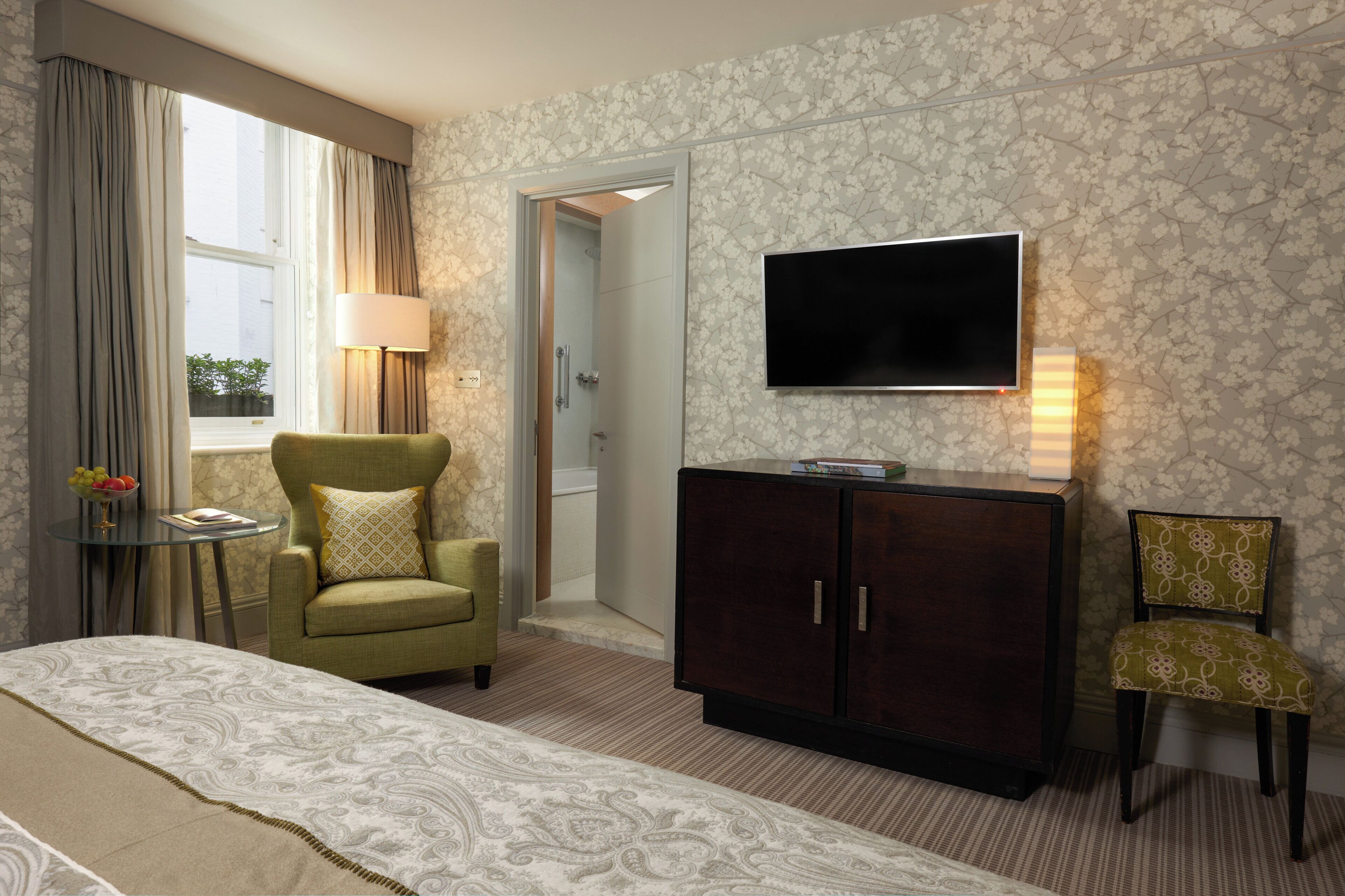 A hotel room with a bed, a seating area with a chair, a television, and a cabinet.