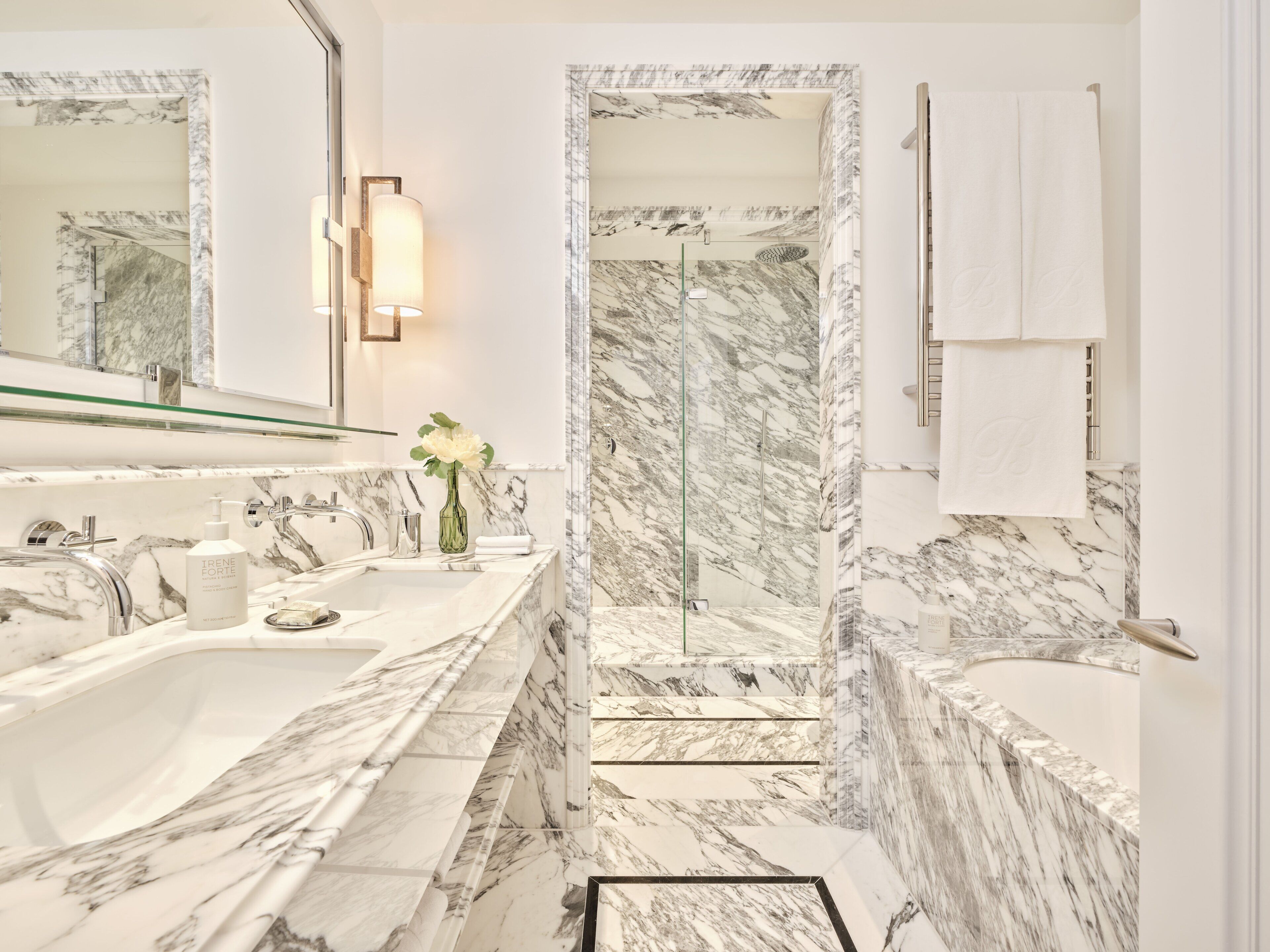 A bathroom with a marble sink, a glass shower enclosure, and a large mirror.