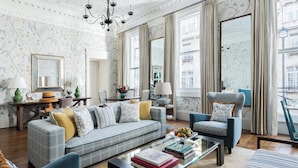 A spacious living room with a sofa, armchairs, and a coffee table. There is a large mirror, a chandelier, and a view of the city through large windows. - Brown's Hotel, a Rocco Forte Hotel (London)