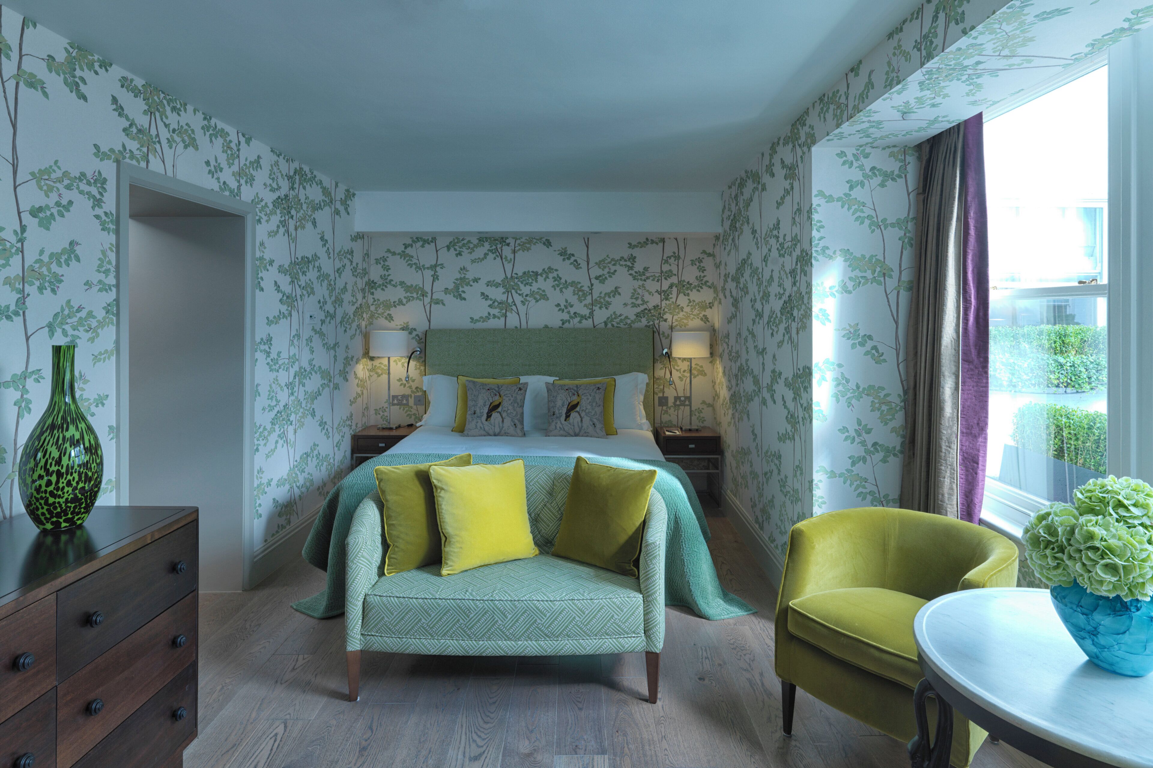 A bedroom with a bed, bedside tables, a dresser, a sofa, a chair, and a window with curtains.