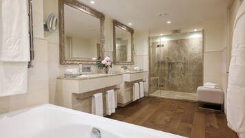 A modern bathroom with a large bathtub, two sinks, a walk-in shower, and a large mirror.