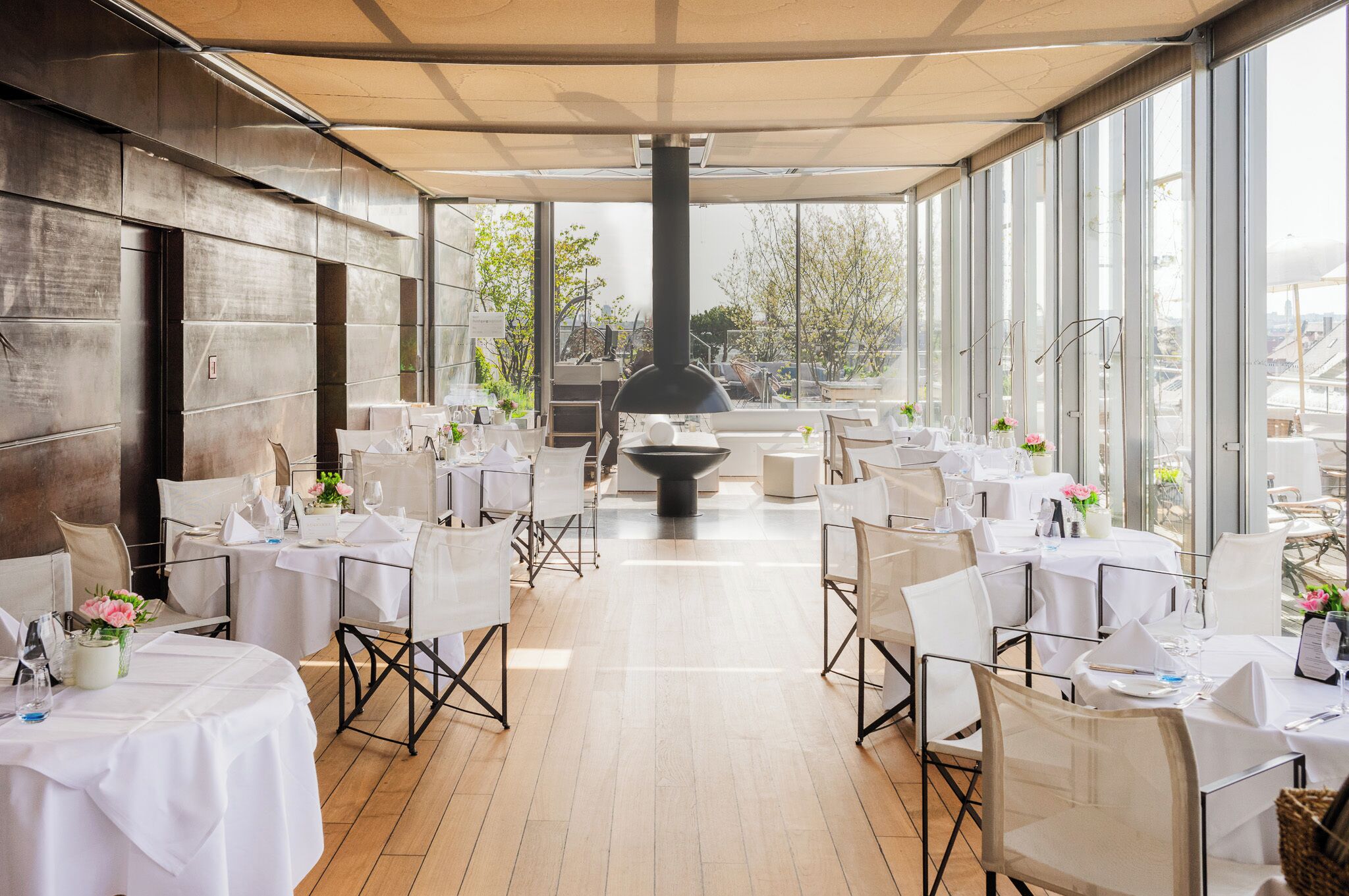 Un restaurante con terraza, mesas dispuestas con manteles blancos y una estufa negra grande en el centro.
