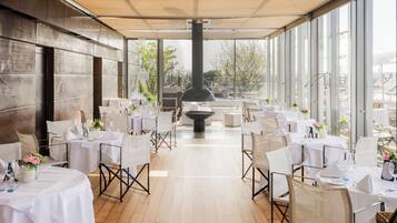 A restaurant with outdoor seating, tables set with white tablecloths, and a large black stove in the center.