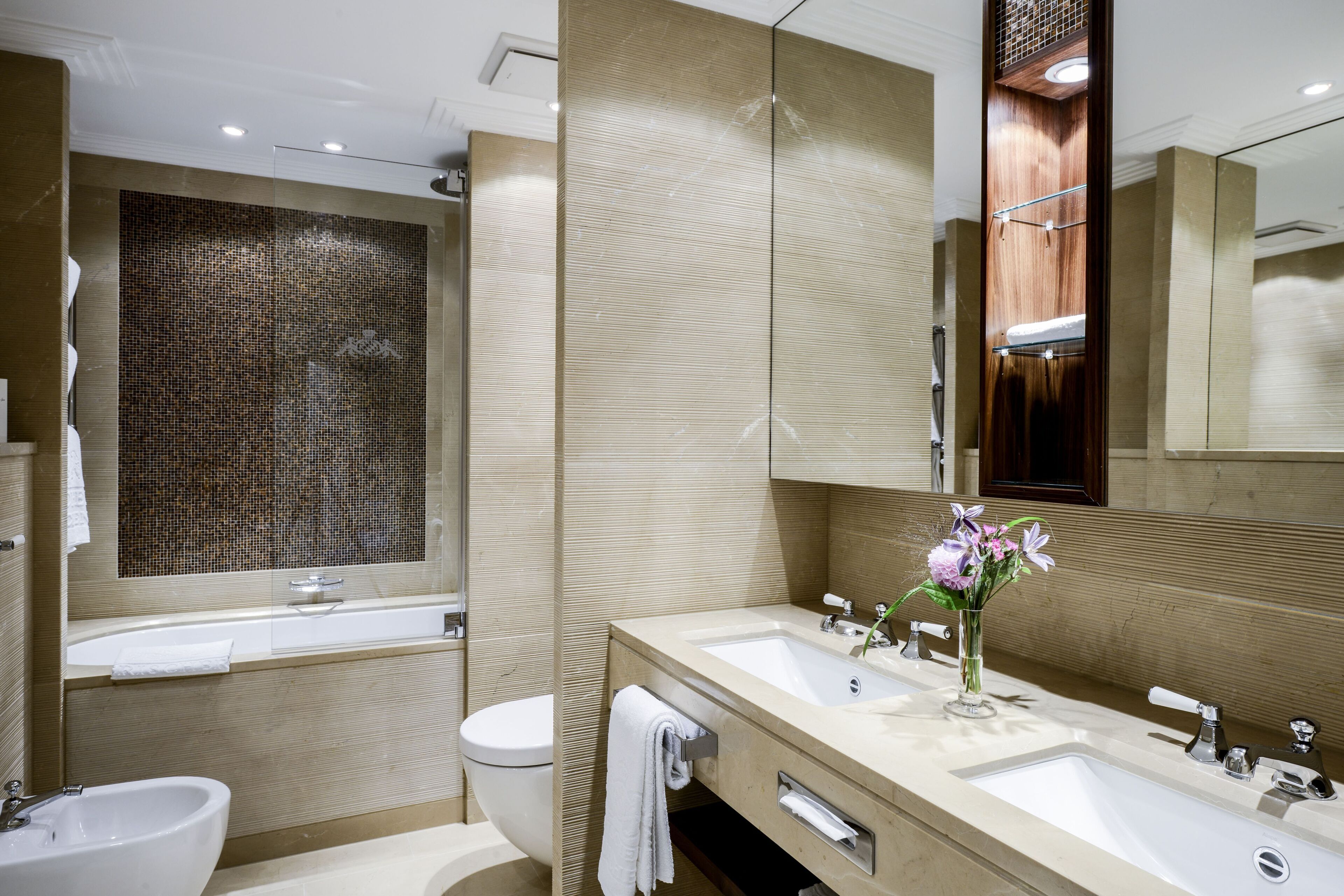 A modern bathroom with a large mirror, two sinks, a bidet, and a shower area.
