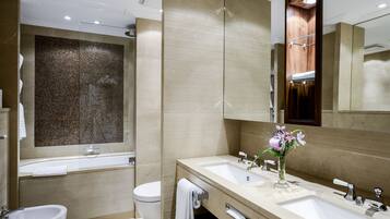 A modern bathroom with a large mirror, two sinks, a bidet, and a shower area.