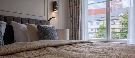 A hotel room with a large bed, a wall-mounted light, and a view of a building with a tower through a window.