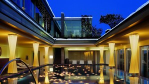 A modern hotel lobby with a central pool area, illuminated by candles and featuring a glass ceiling. - Hotel Bayerischer Hof - The Leading Hotels of the World (Munich)
