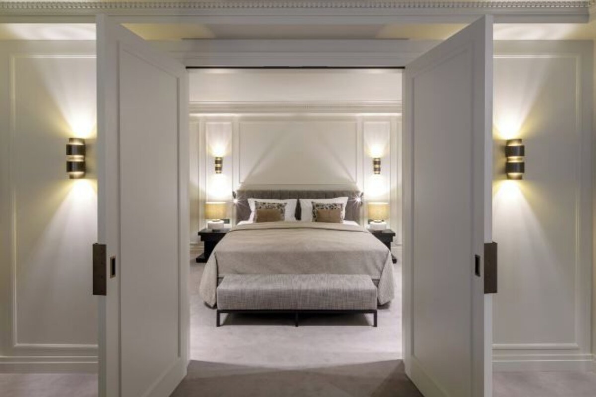 A bedroom with a large bed, two bedside tables, and wall-mounted lighting.