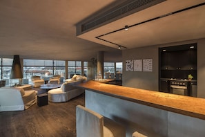 A modern living room with a wooden bar, comfortable seating, and a view of the city.