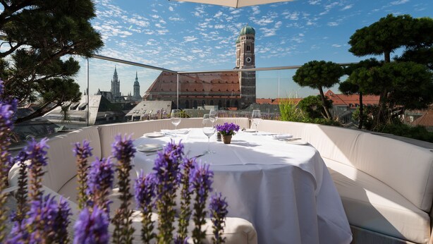 An outdoor dining area with a table set for two, overlooking a historic building with a clock tower. - Hotel Bayerischer Hof - The Leading Hotels of the World (Munich)