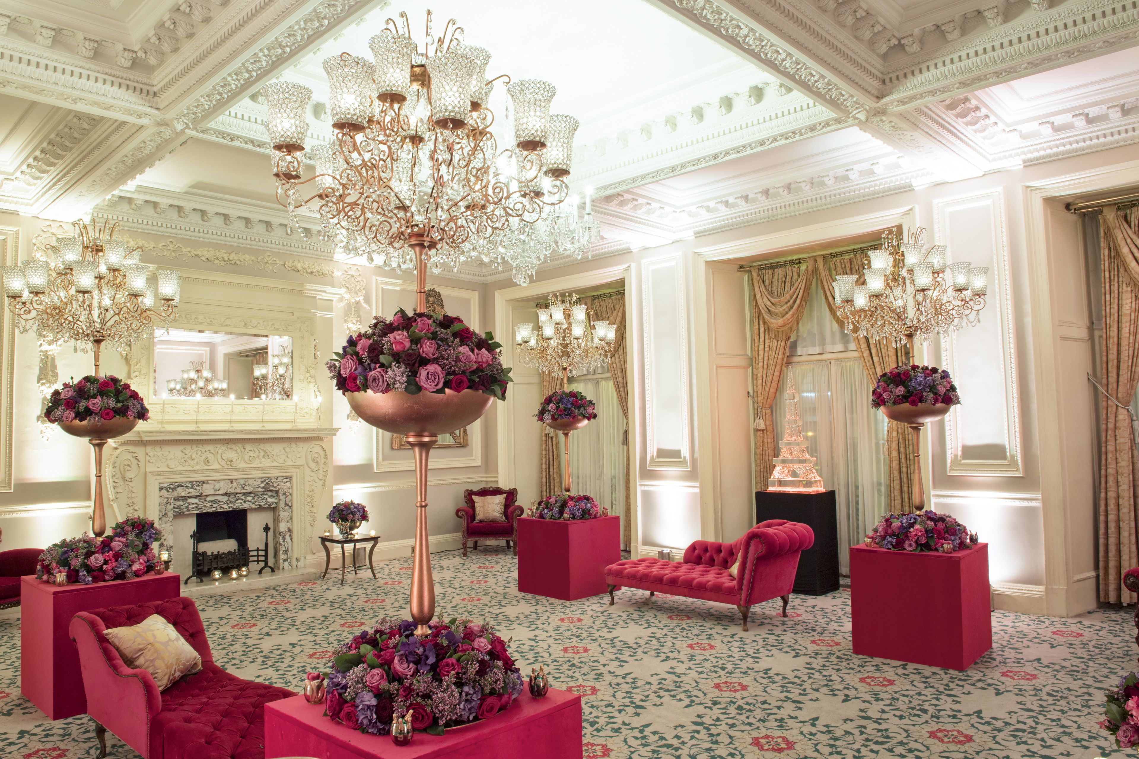 A luxurious room with ornate chandeliers, red upholstered furniture, and floral arrangements.