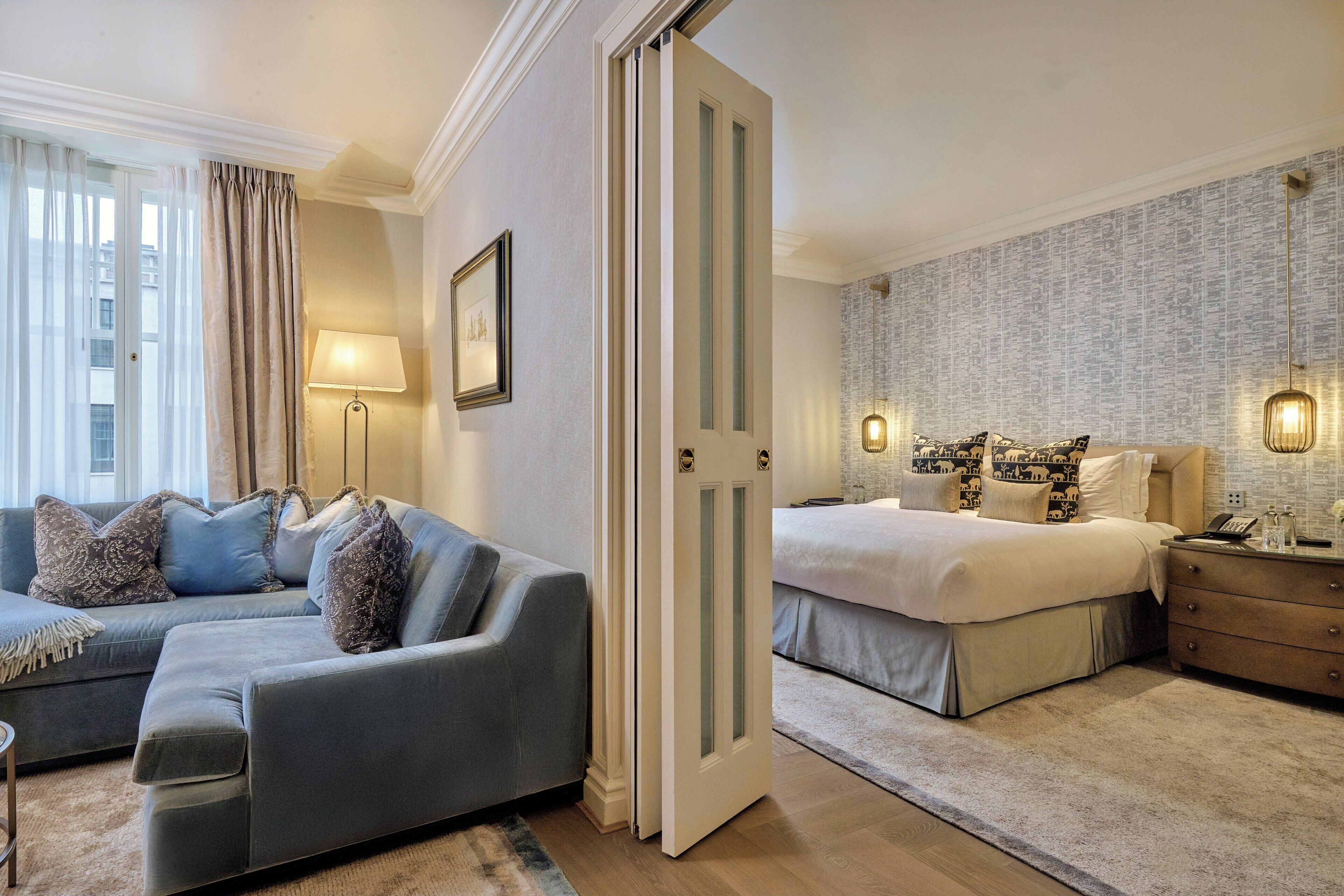 Habitación de hotel con sofá, cama, mesita de noche y pared con estampado de periódico.