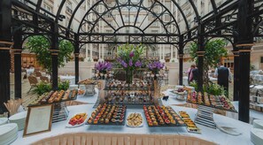 A banquet hall with a central floral arrangement, surrounded by tables with various desserts and a menu sign. - The Landmark London (London)