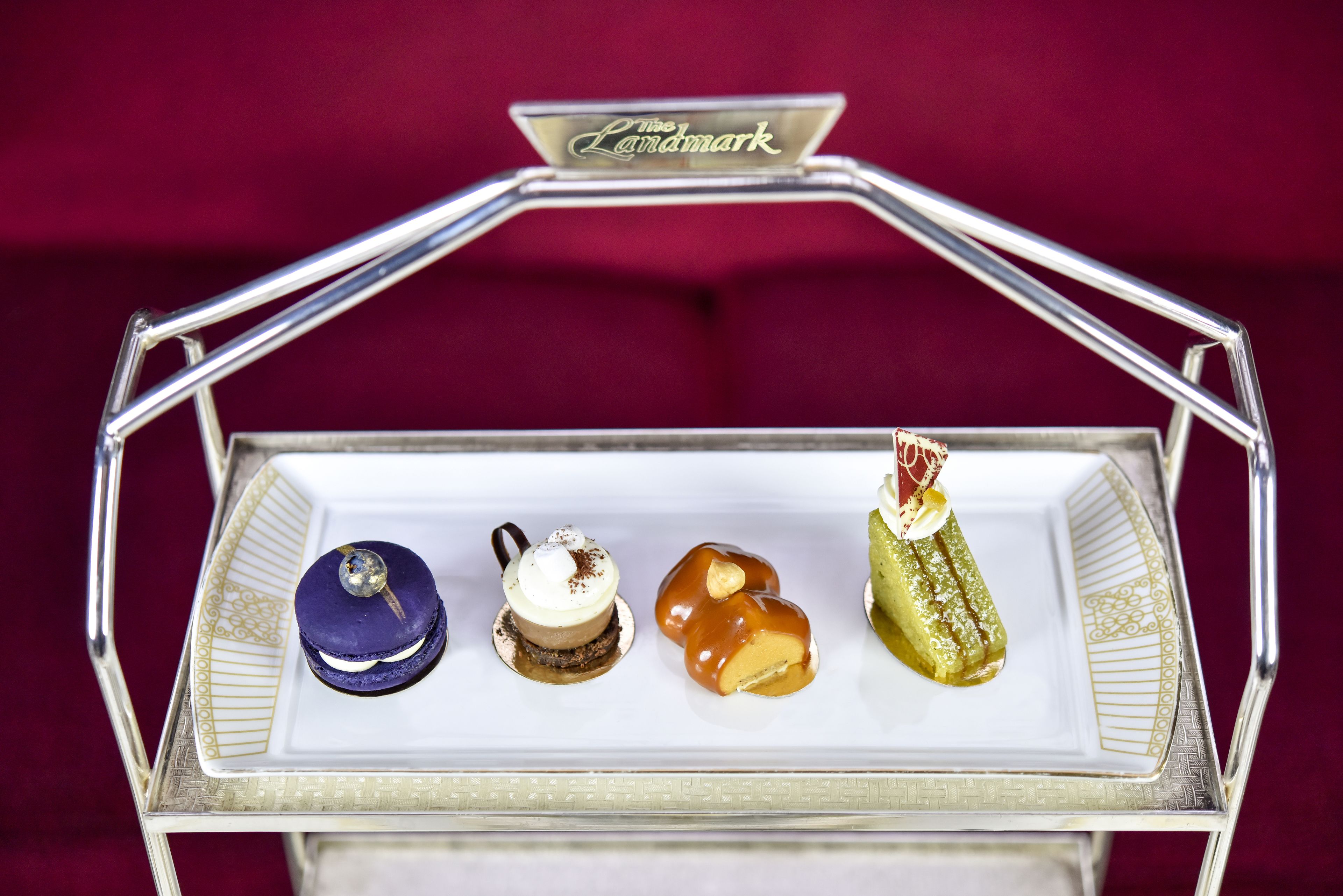 A dessert display with four different types of desserts on a white plate, set on a silver tray with a 'Landmark' sign above.