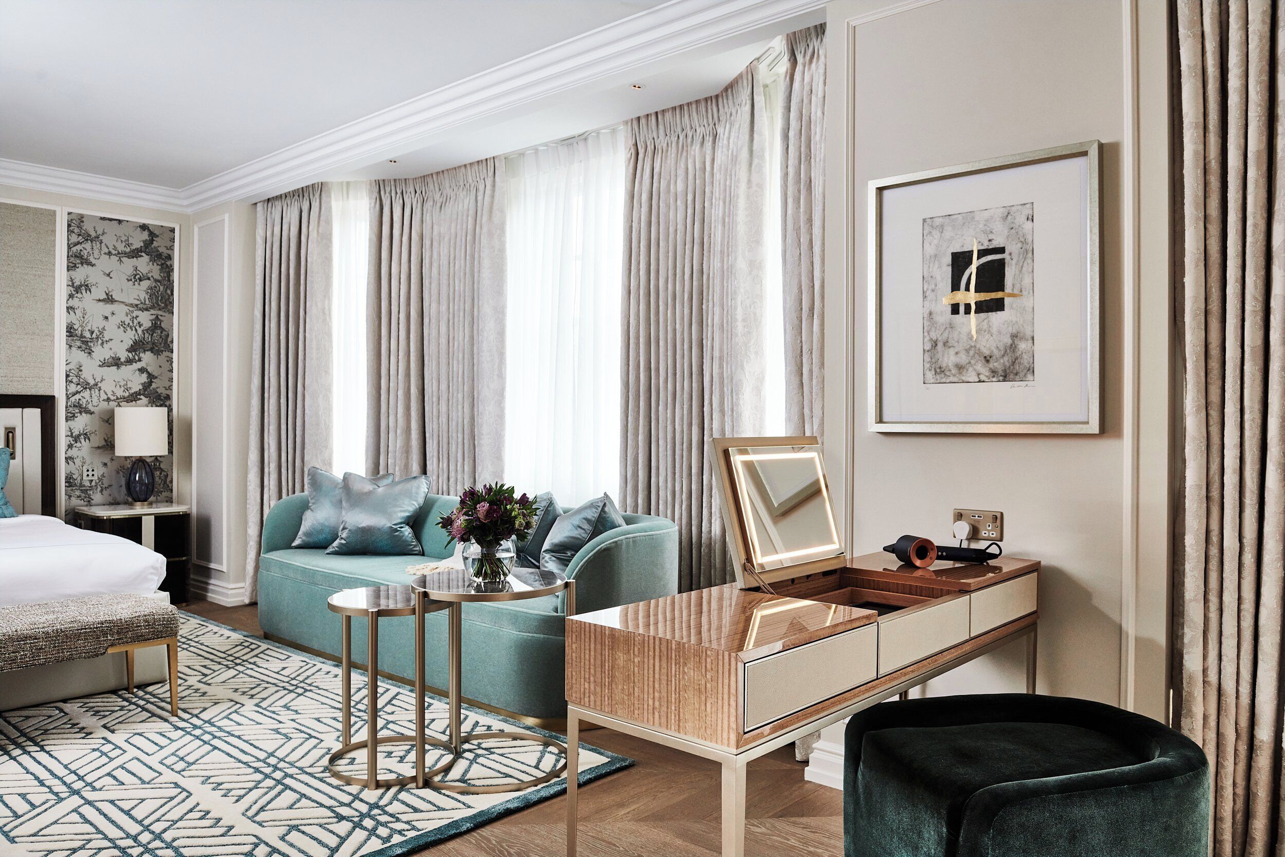 A modern hotel room with a bed, a sofa, a desk with a mirror, and a chair.
