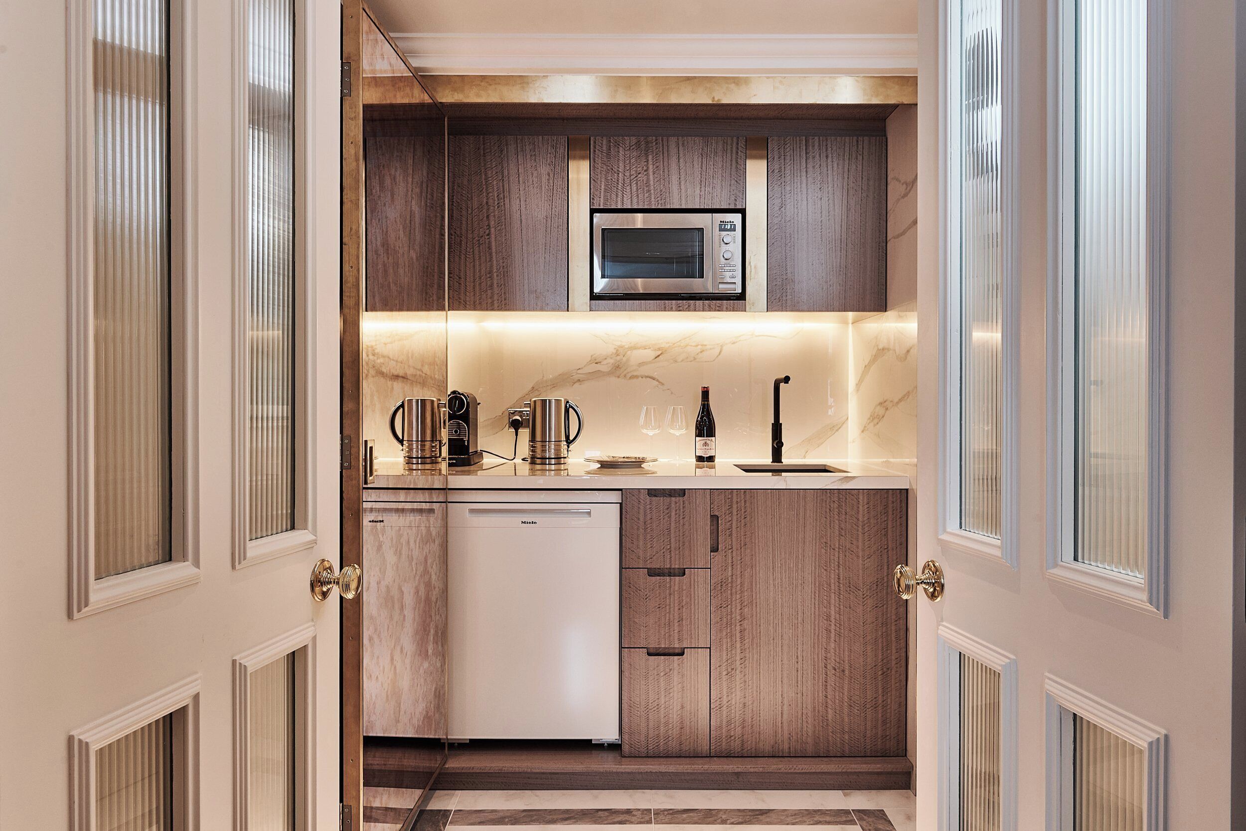 A compact kitchen with a built-in microwave, a dishwasher, and a wine bottle on the counter.