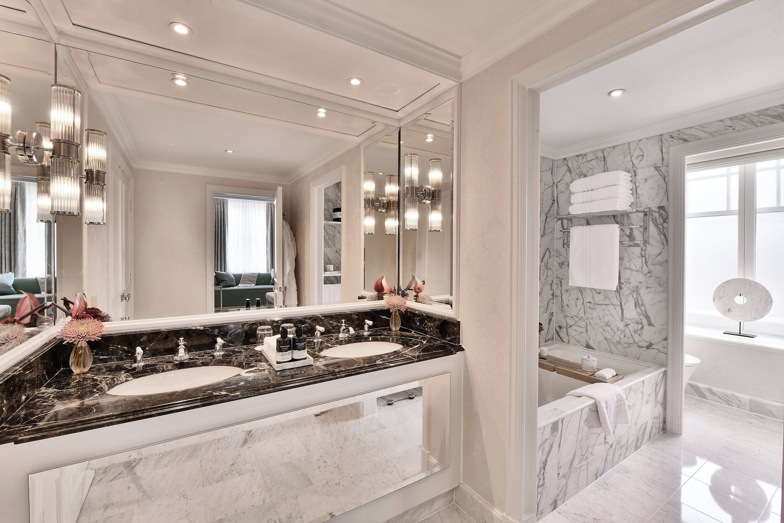 A luxurious bathroom with a large mirror, two sinks, marble countertops, and a bathtub.