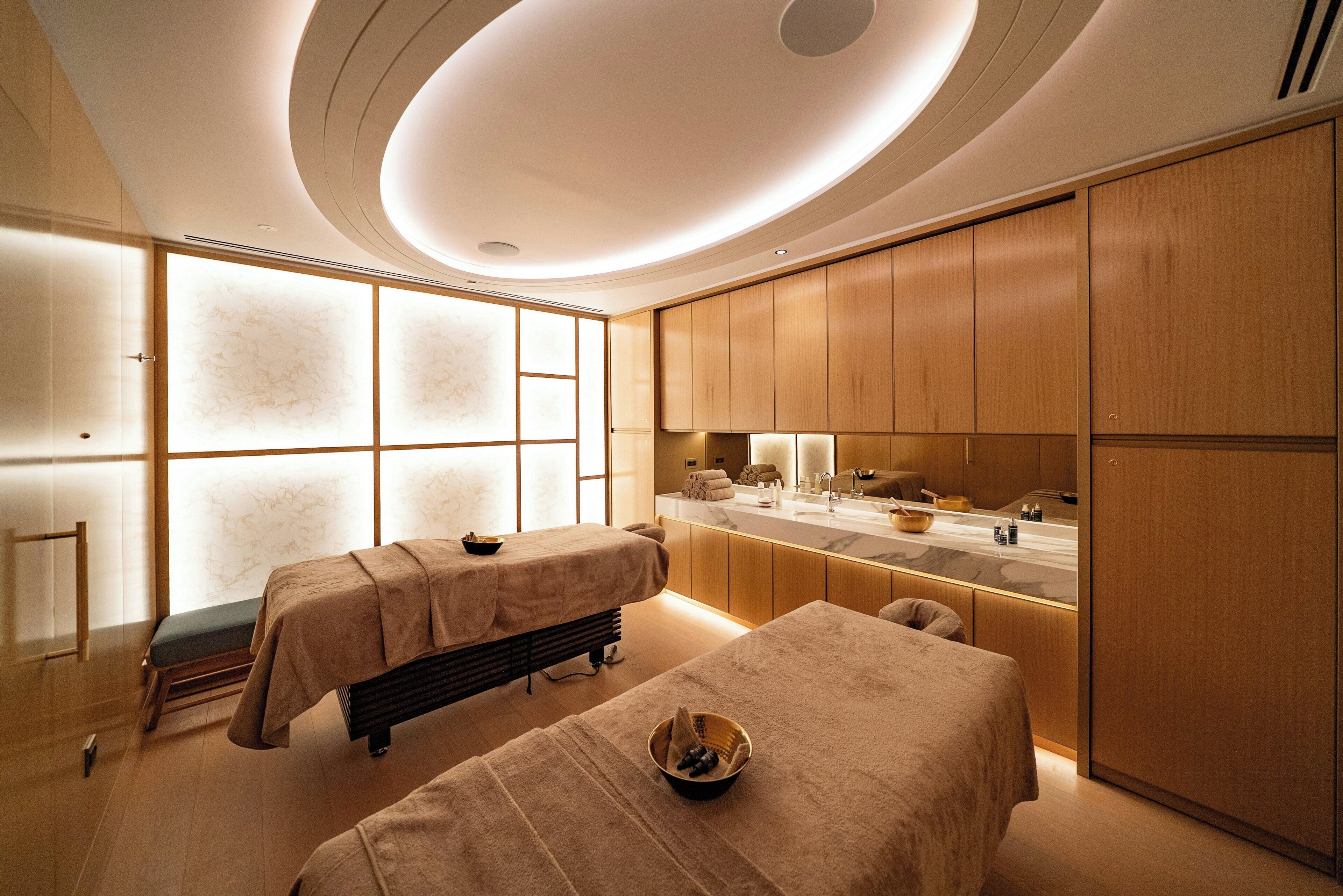 Un cuarto de spa con dos camillas, un espejo grande y un armario de madera.