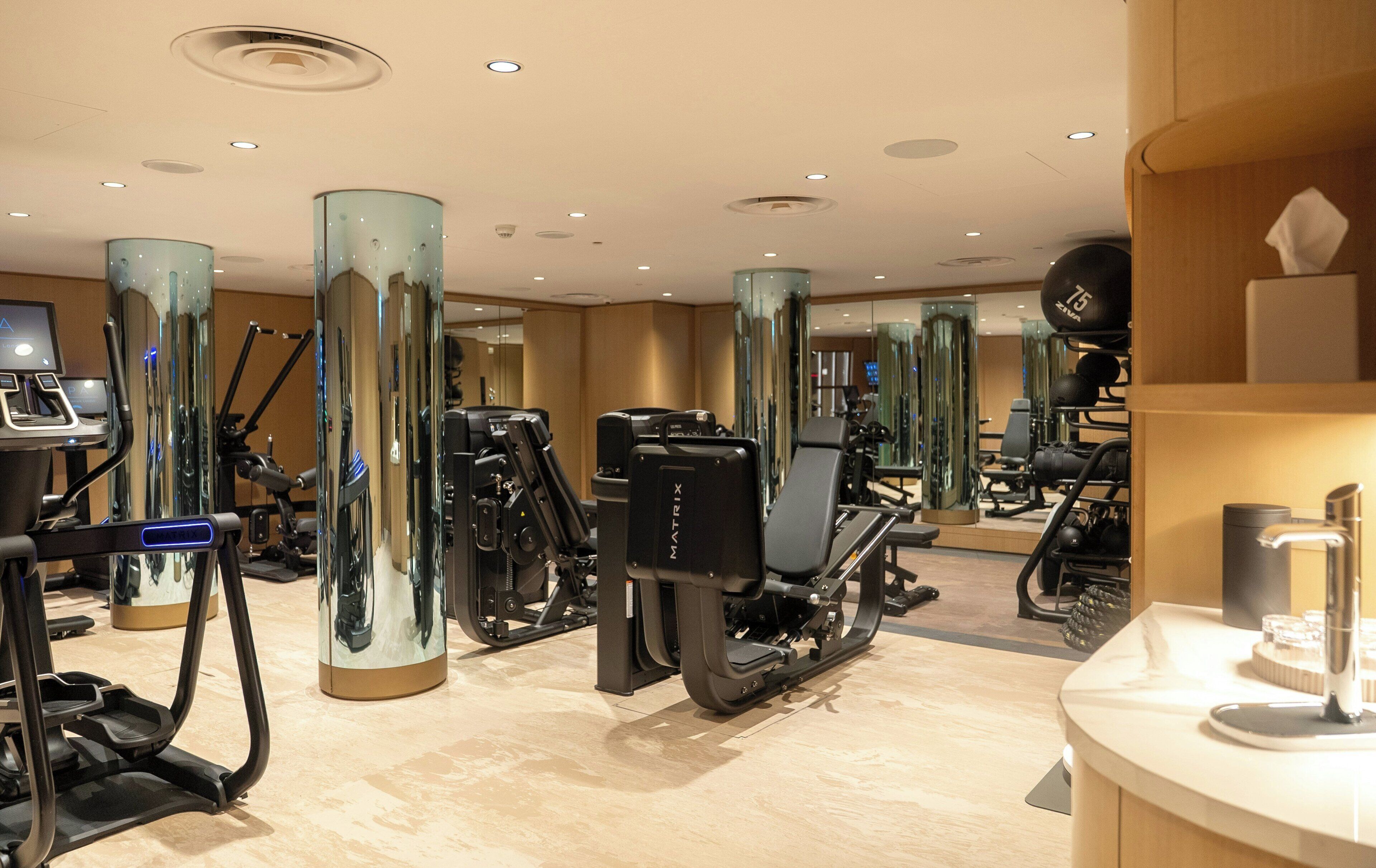 A gym with various exercise equipment, including treadmills and weight machines, and a mirror wall reflecting the space.