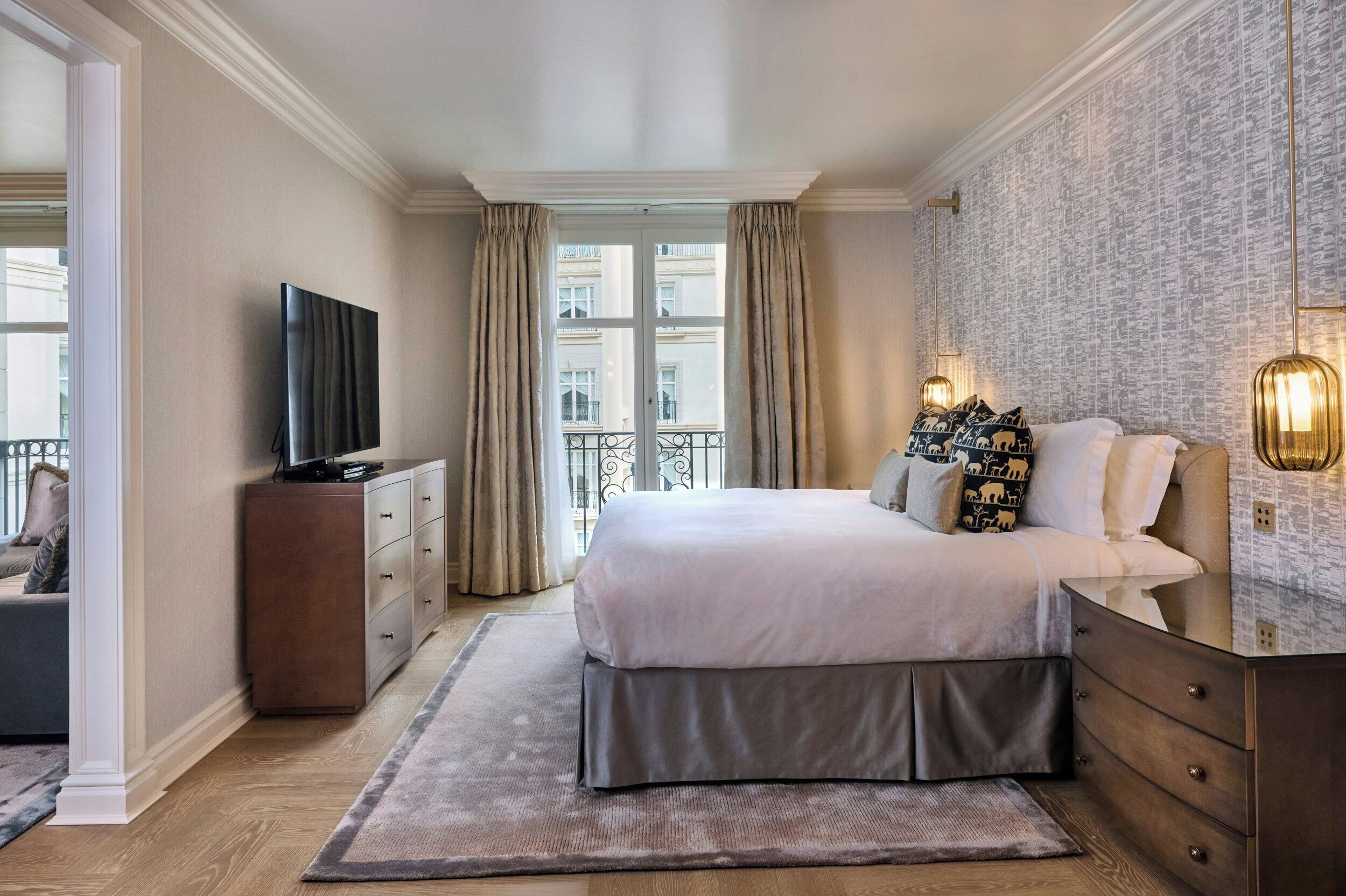 A bedroom with a bed, a TV, a dresser, and a window with curtains.
