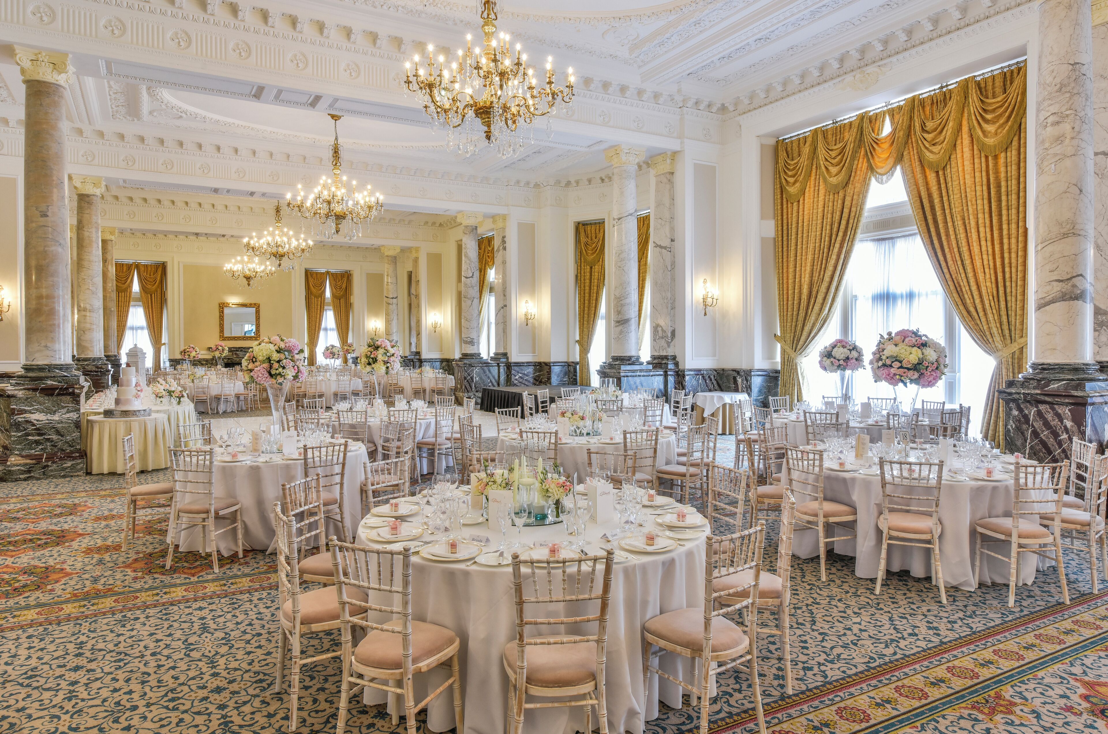 A grand banquet hall with round tables, elegant chandeliers, and classical architecture.