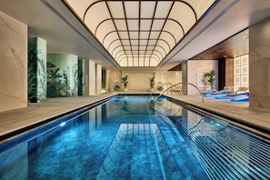 A swimming pool with a glass bottom, surrounded by a modern interior with a high ceiling and a geometric light fixture.
