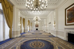 A grand hallway with a large chandelier, ornate blue and gold carpet, and a fireplace on the right. - The Landmark London (London)