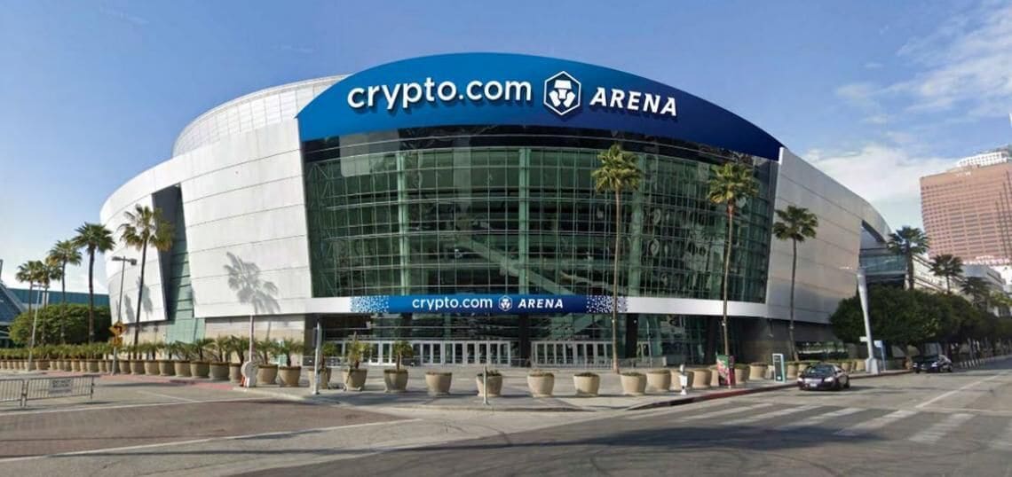 A modern building with a curved facade, large glass windows, and a prominent sign reading "crypto.com ARENA".