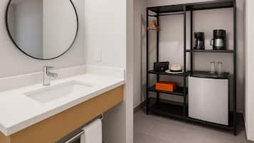 A modern bathroom with a white sink, a round mirror, and a black shelving unit with a coffee maker and a box.