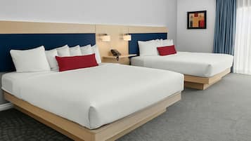 A hotel room with two beds, a headboard with a blue and beige color scheme, a bedside table with a lamp, and a framed picture on the wall.
